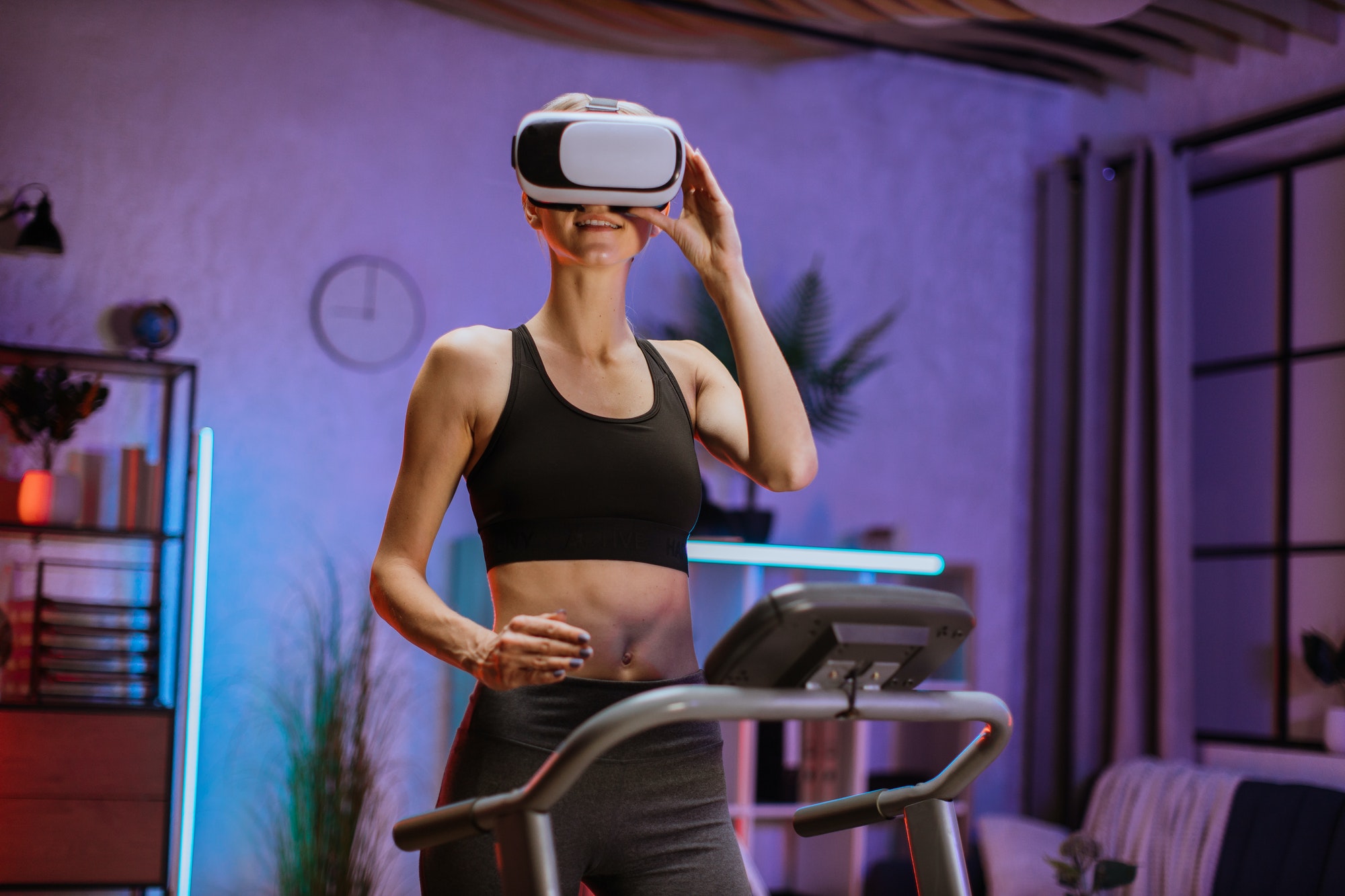 Sporty blond caucasian woman in grey sportswear and headphones training at home using vr glasses